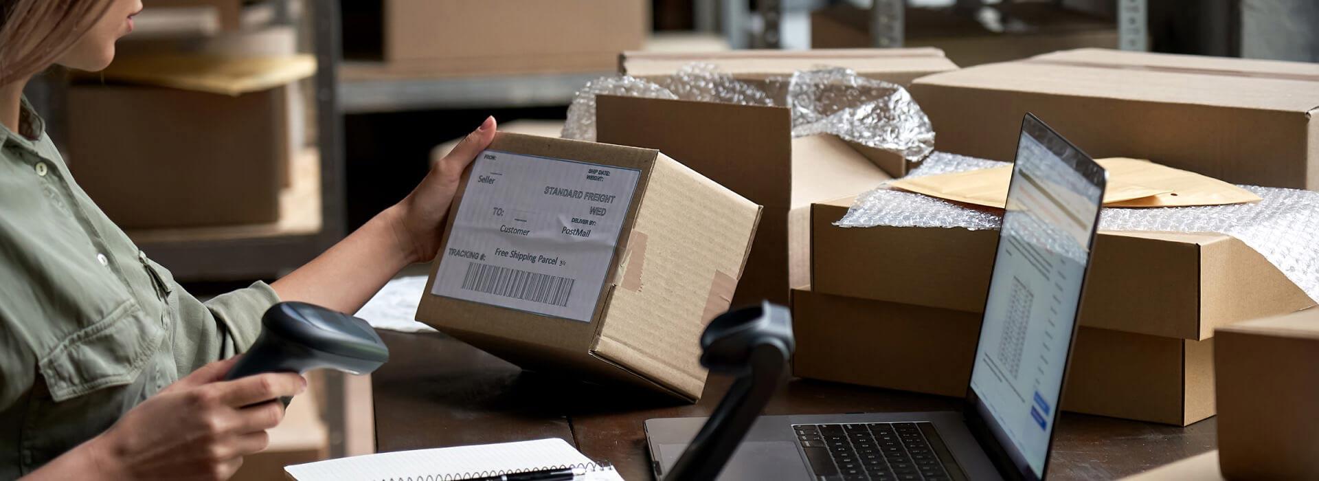 Woman scanning a shipping label amidst boxes in a warehouse setting