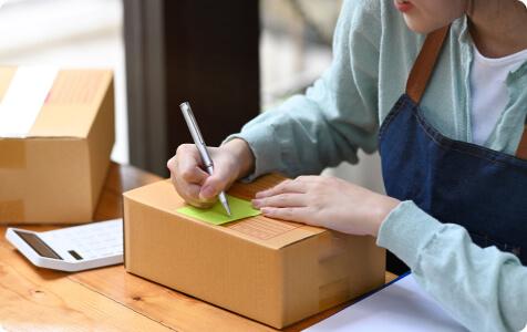 A person in an apron writing on a sticky note attached to a cardboard box